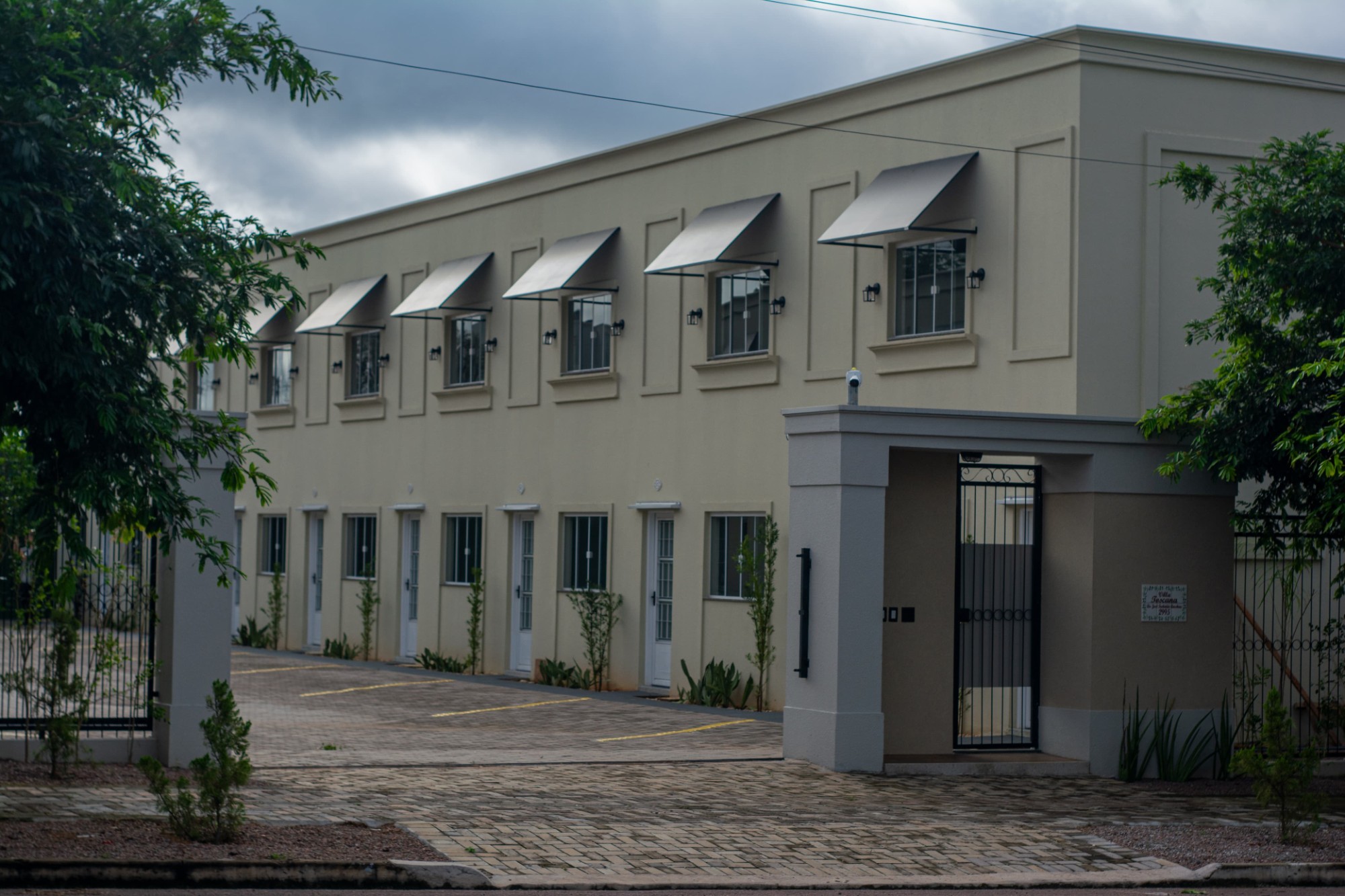 Condomínio Villa Toscana: prédio de lofts de dois pavimentos, com toldos nas janelas, estacionamento interno e portão de entrada
